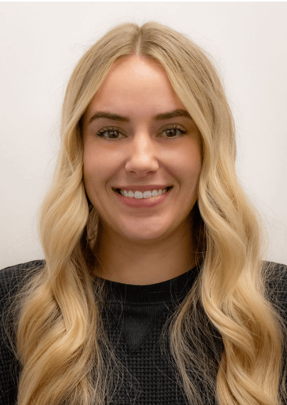 Headshot of a smiling young woman with long blonde hair, a septum piercing, and a gold cross necklace.